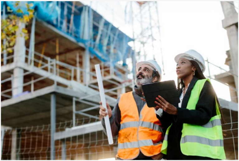 Two construction workers in hard hats and safety vests at a building site