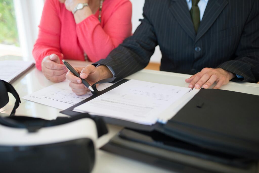 A lawyer in a suit reviews and points to legal documents with a woman, discussing paperwork at a desk.