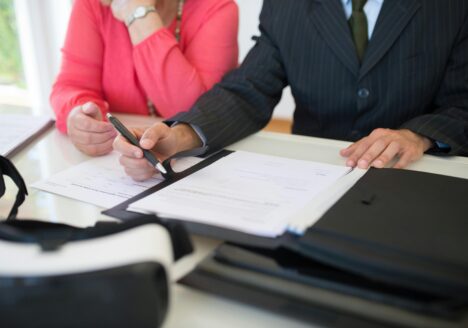 A lawyer in a suit reviews and points to legal documents with a woman, discussing paperwork at a desk.