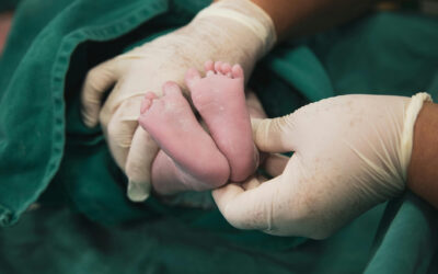 Doctor wearing surgical gloves gently holding a newborn’s feet in a delivery room, representing careful medical attention during childbirth.