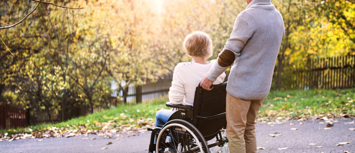 A caregiver assisting an adult wheelchair user outdoors, symbolizing support and life after hospital discharge.