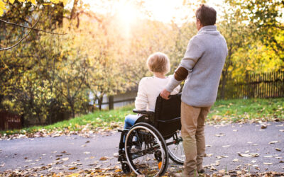 A caregiver assisting an adult wheelchair user outdoors, symbolizing support and life after hospital discharge.