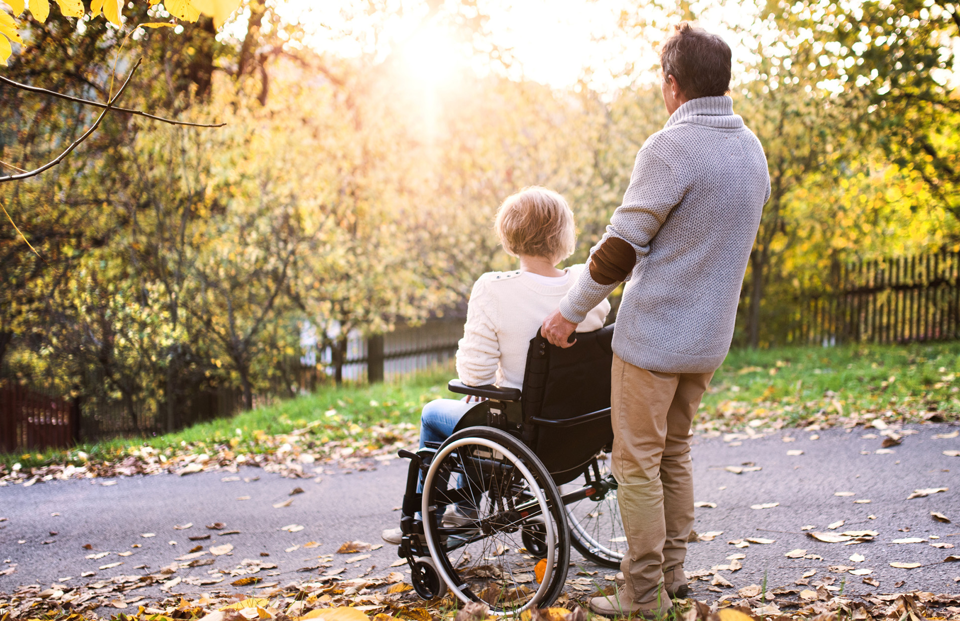 A caregiver assisting an adult wheelchair user outdoors, symbolizing support and life after hospital discharge.