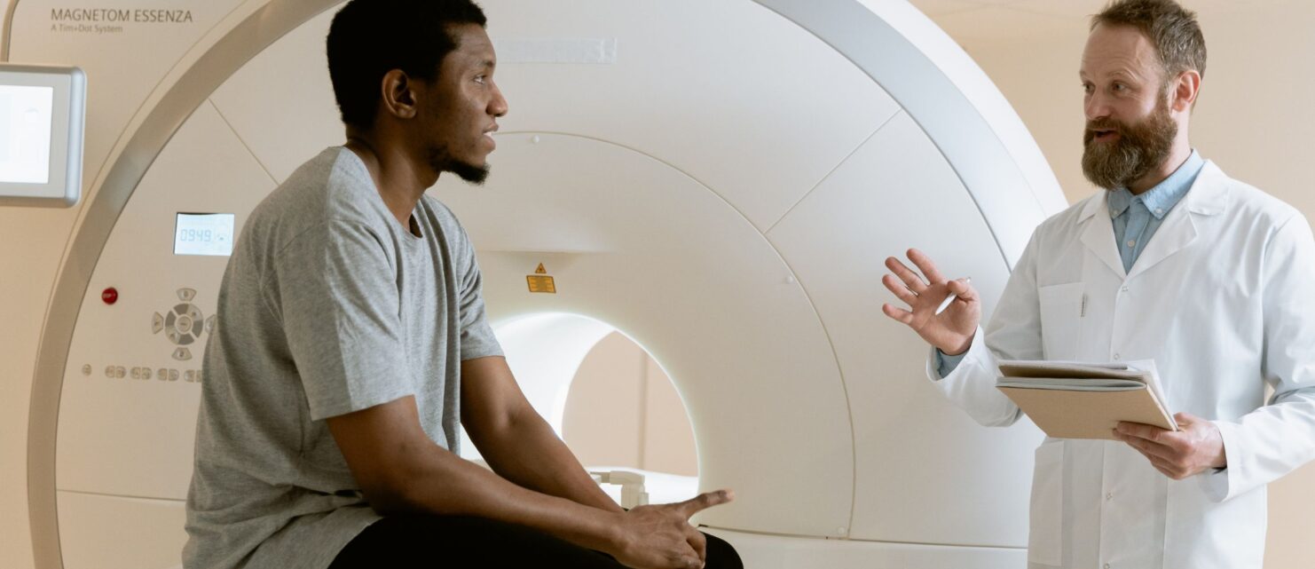 A doctor speaking with a patient seated on an MRI machine before a diagnostic brain scan.