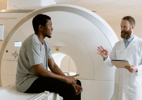 A doctor speaking with a patient seated on an MRI machine before a diagnostic brain scan.