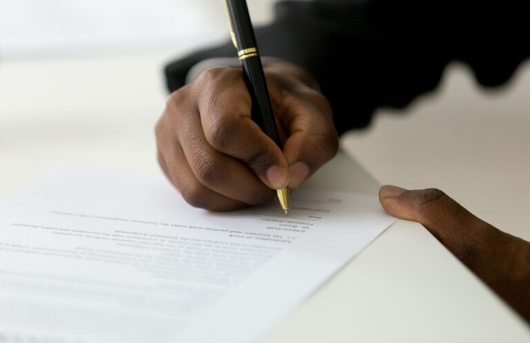 Hand signing policy paperwork, representing insurance coverage decisions.