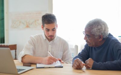 Long-term care funding after a traumatic brain injury Younger family member helping an older man work through benefit paperwork at a desk, representing the process of assembling funding for long-term care after a TBI