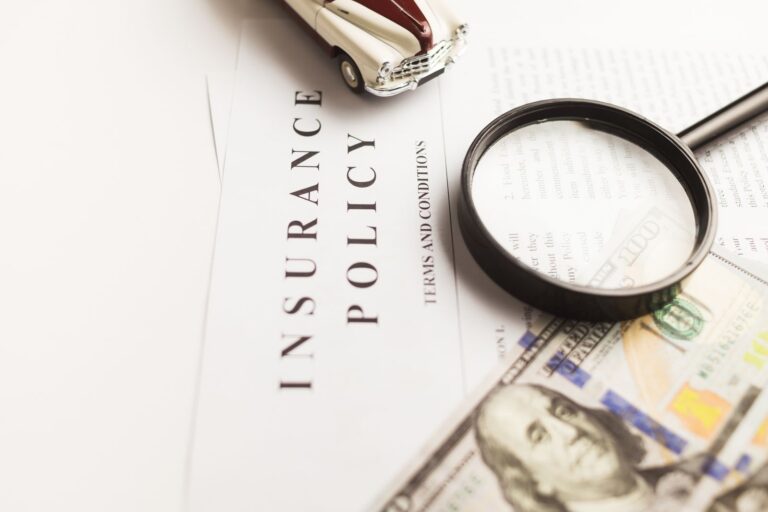 Magnifying glass over an auto insurance policy with a toy car, representing PIP and UM/UIM coverage after a TBI crash